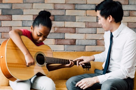 Child learning guitar from adult instructor
