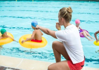 Swimming instructor on side of pool giving instructions to children in the pool 