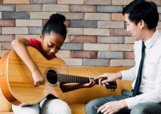 an adult teaching a child to play guitar