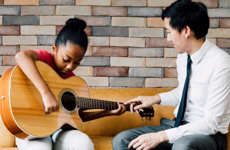 an adult teaching a child to play guitar