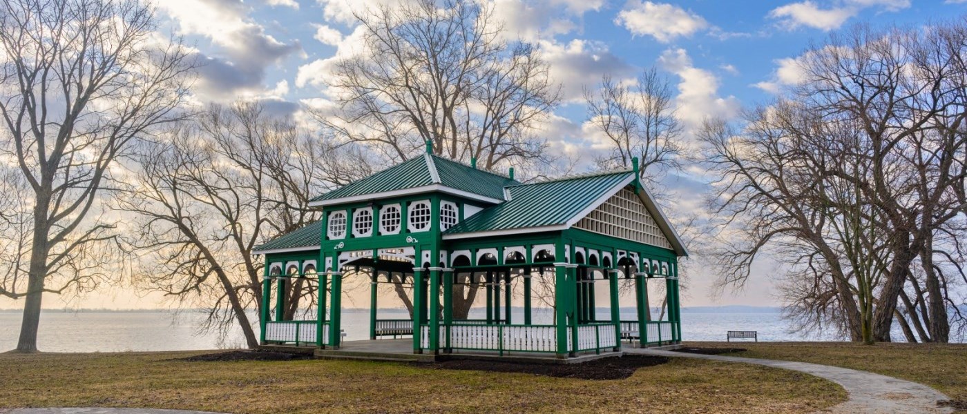 bare branched trees on a shoreline in winter with a green and white pavilion 