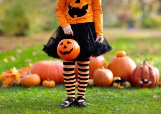 Little girl in halloween costume with pumpkins behind