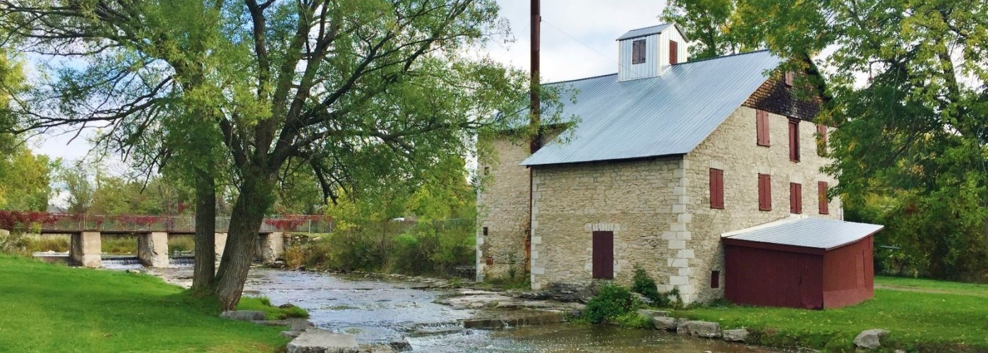 A historic mill building on a stream with trees in leaf