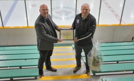 man giving award to another in front of ice rink