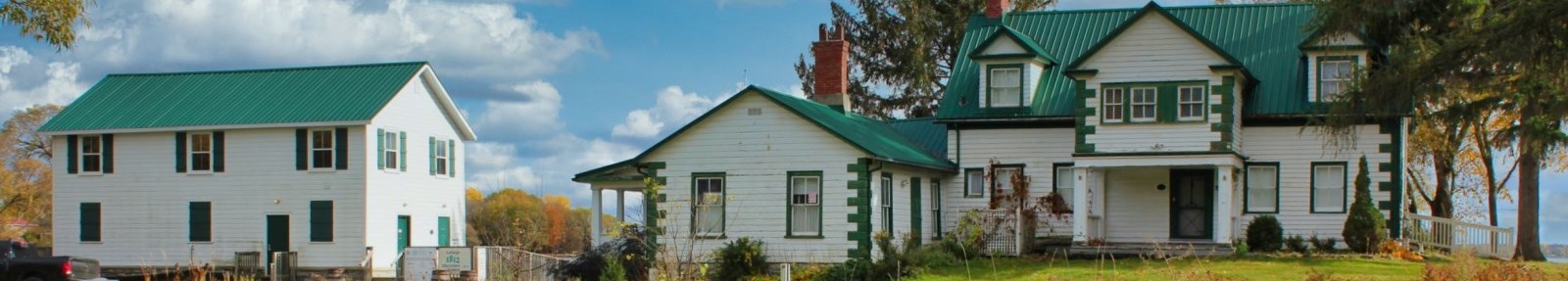 old white clapboard house with green roof at lakeshore with a jetty