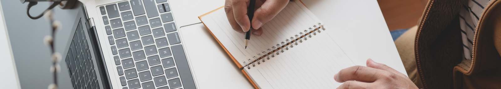 laptop with hands writing in a notepad