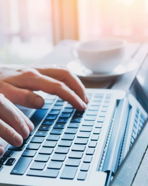 Person typing on a laptop with coffee cup in background