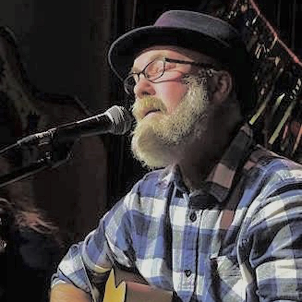 man with beard singing and playing a guitar