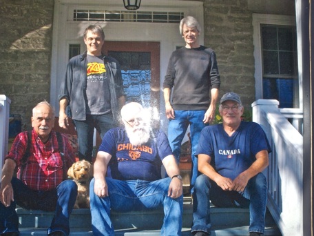five men posing standing and sitting at the top of steps to deck