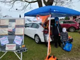 Woman and young boy standing dressed in costumes standing under a blue canopy, in front of the back of a white car.