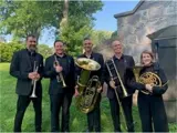 5 people dressed in all black holding brass instruments outside.