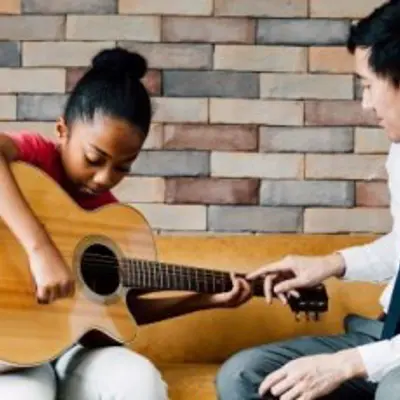 an adult teaching a child to play guitar